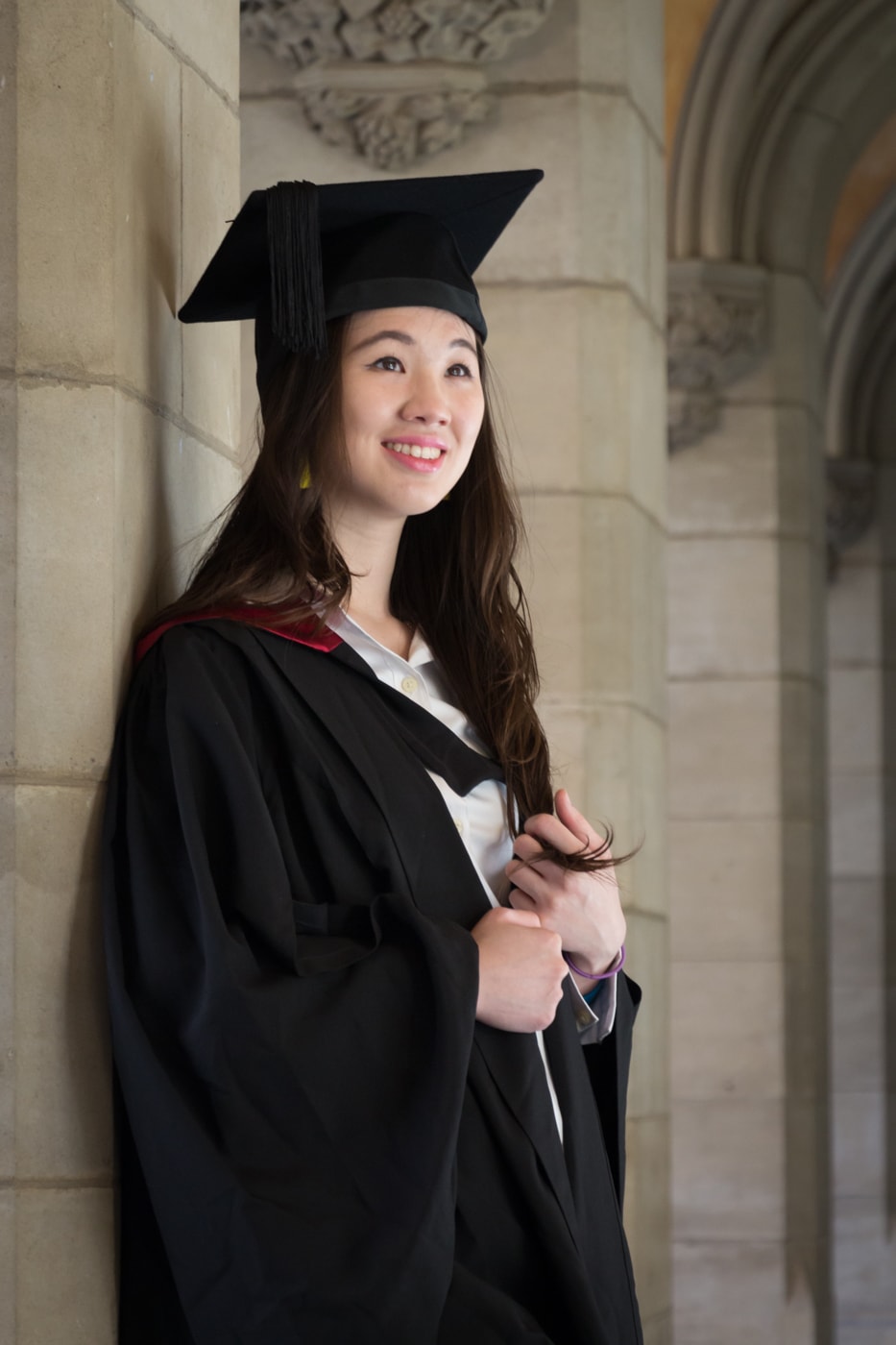 QUT graduate learning against wall wearing graduation gown